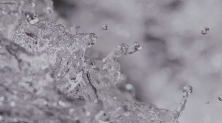 Close-up of water splashing, capturing droplets and ripples in motion against a gray background, highlighting the essence of clean water.