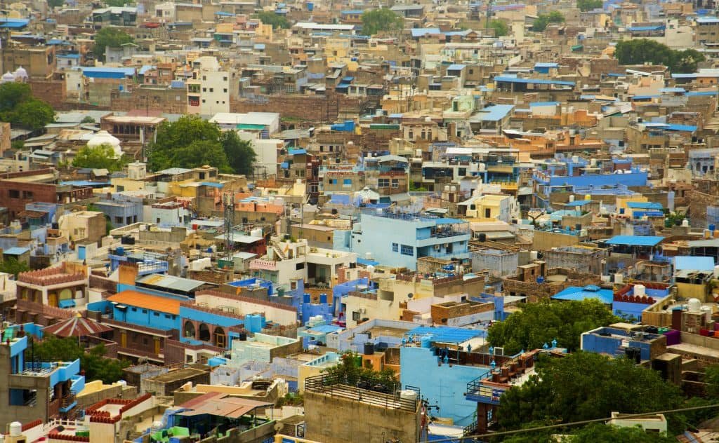Aerial view of a densely packed city with numerous buildings, many painted in shades of blue, surrounded by a few green trees.