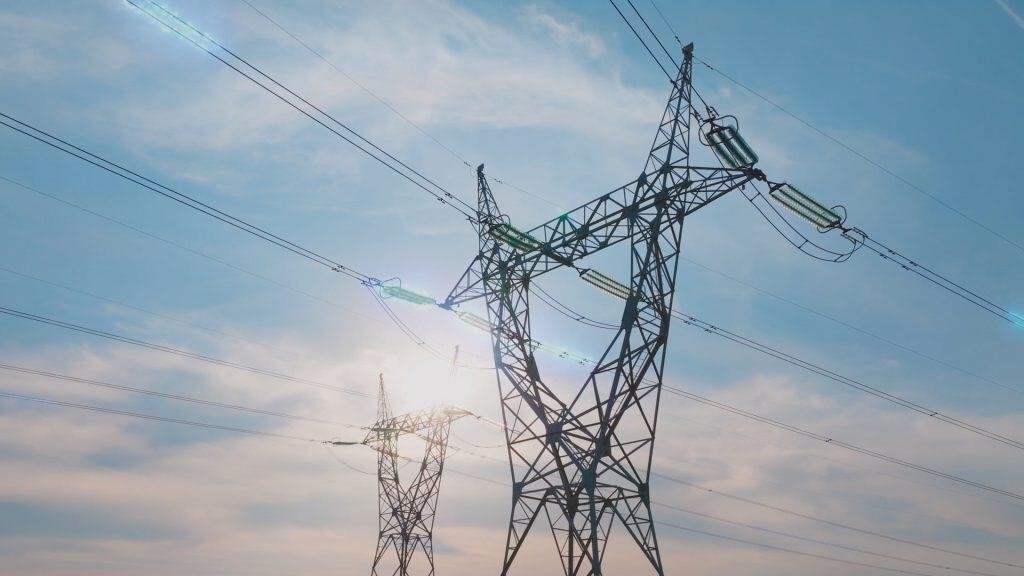 Transmission towers and power lines against a blue sky with clouds and sunlight.