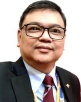 A man named Aung Thet Paing, wearing glasses and a suit with a tie, proudly displays a small flag pin on his lapel.