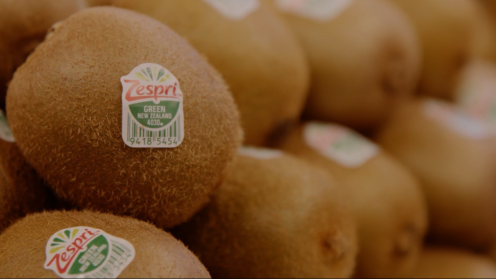 Close-up of kiwi fruits with Zespri labels stacked in piles.
