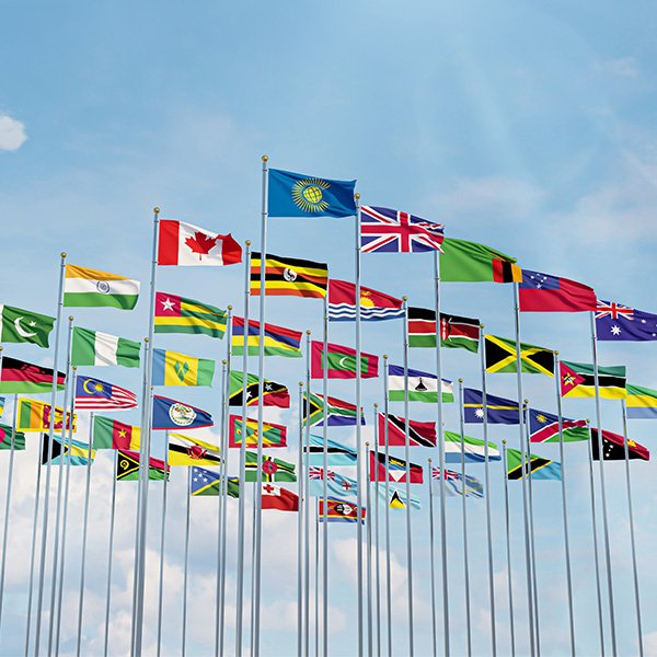 Multiple national flags and the Commonwealth flag are displayed on tall flagpoles against a blue sky with some clouds, celebrating the Commonwealth 75 anniversary.