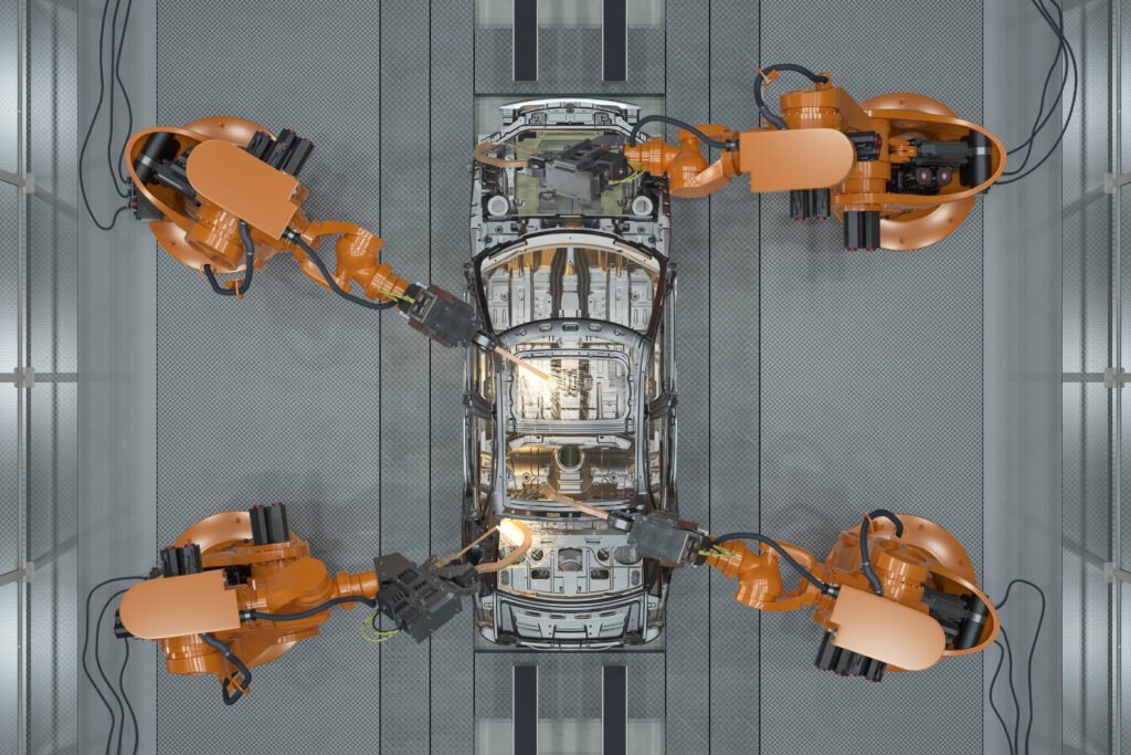 Four robotic arms assemble or weld a car frame on an automated production line in a factory, viewed from above.