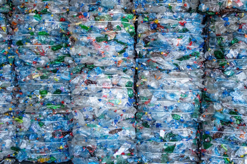 Bales of compressed plastic bottles stacked together for recycling, with various colored caps and mixed plastics visible.