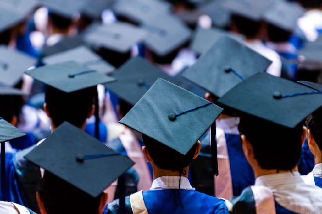 A group of graduates seen from behind, wearing caps and gowns, gathered at a graduation ceremony.